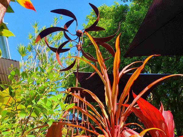 Large metal wind mill surrounded by plants